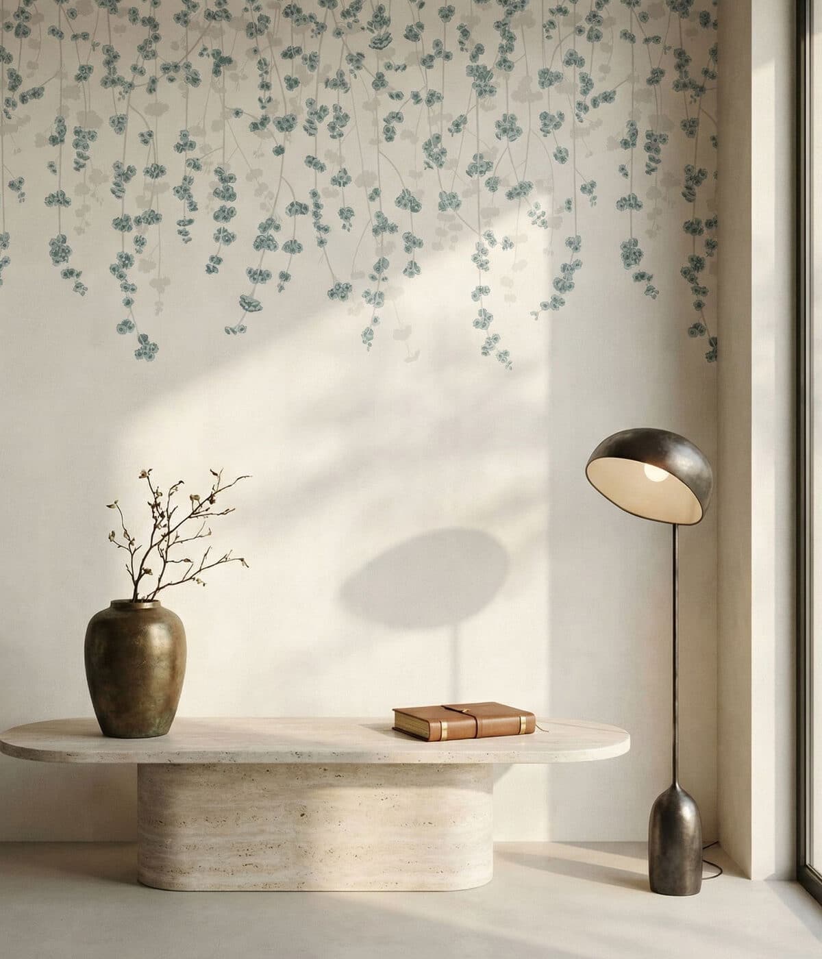 A minimalist interior featuring delicate white wallpaper with soft blue hanging blossom patterns. A sculptural stone bench holds a ceramic vase with branches and a small notebook, while a modern floor lamp and natural sunlight create a calm, serene atmosphere.
