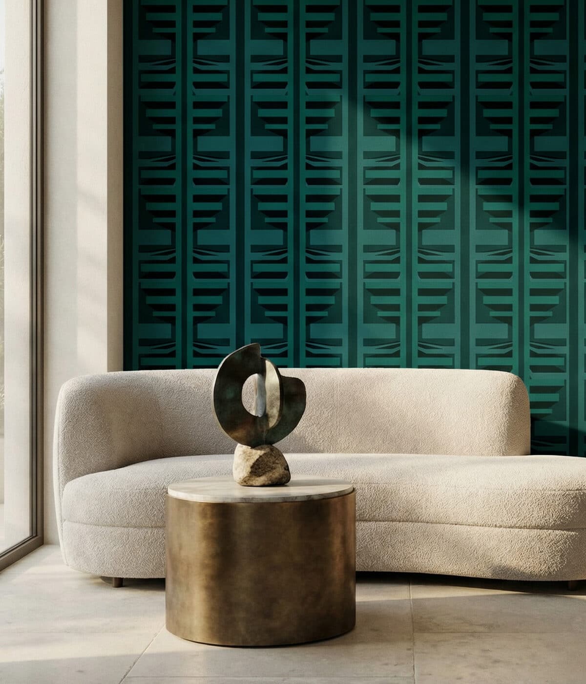 A modern living room with a curved cream boucle sofa placed in front of a deep green geometric wallpaper featuring a repeating layered pattern. In front of the sofa sits a round metal coffee table with a light stone top, displaying a sculptural abstract art piece mounted on a small stone base. Natural light from a nearby window casts soft shadows across the wall and furniture, highlighting the bold, textured backdrop.