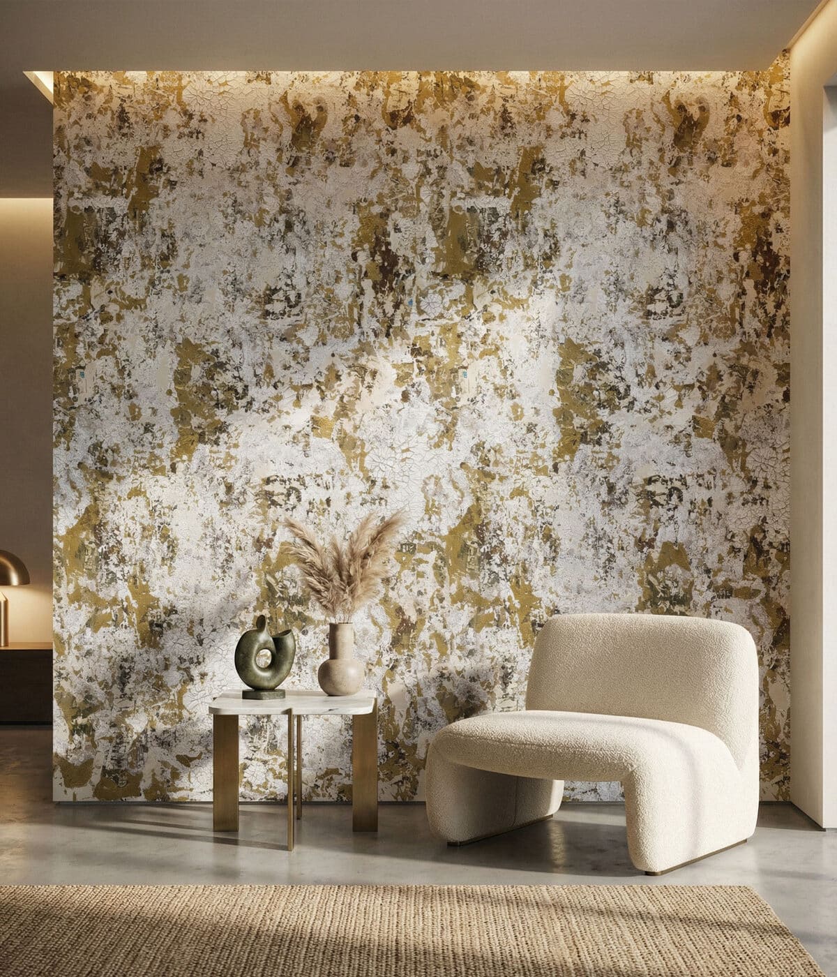 A modern interior featuring abstract gold and white textured wallpaper with a distressed, artistic finish. A sculptural cream lounge chair sits beside a small marble-top side table with decorative objects and dried grasses, creating a warm and sophisticated space.
