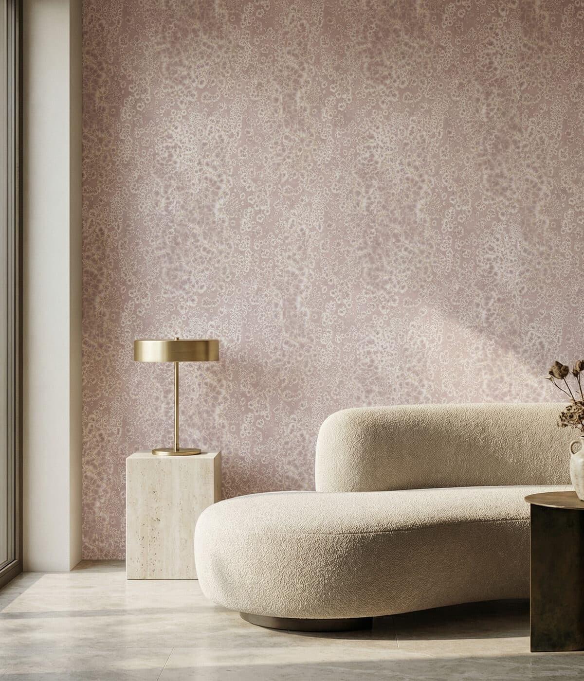 A contemporary living space featuring soft pink abstract wallpaper with delicate organic patterns. A curved cream sofa sits beside a stone pedestal table with a brass lamp, while warm sunlight creates gentle shadows across the minimalist interior.