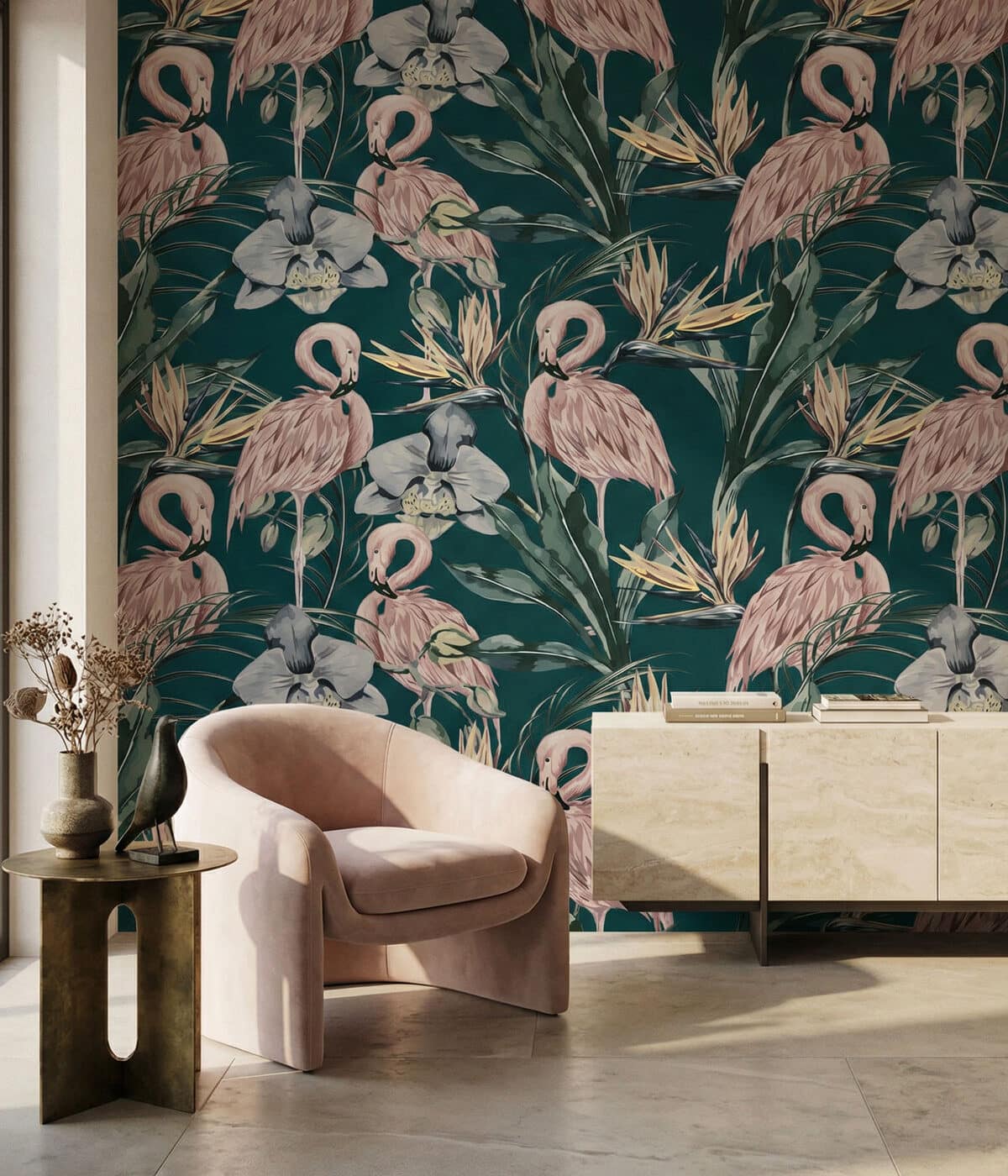 A modern interior featuring a soft blush-pink upholstered lounge chair beside a small round brass side table holding decorative vases and a bird sculpture. Behind it, a dark green tropical wallpaper displays a repeating pattern of pink flamingos, large orchids, and lush foliage. To the right, a light stone sideboard with books sits against the wall, while sunlight from a nearby window casts warm shadows across the floor and furniture.