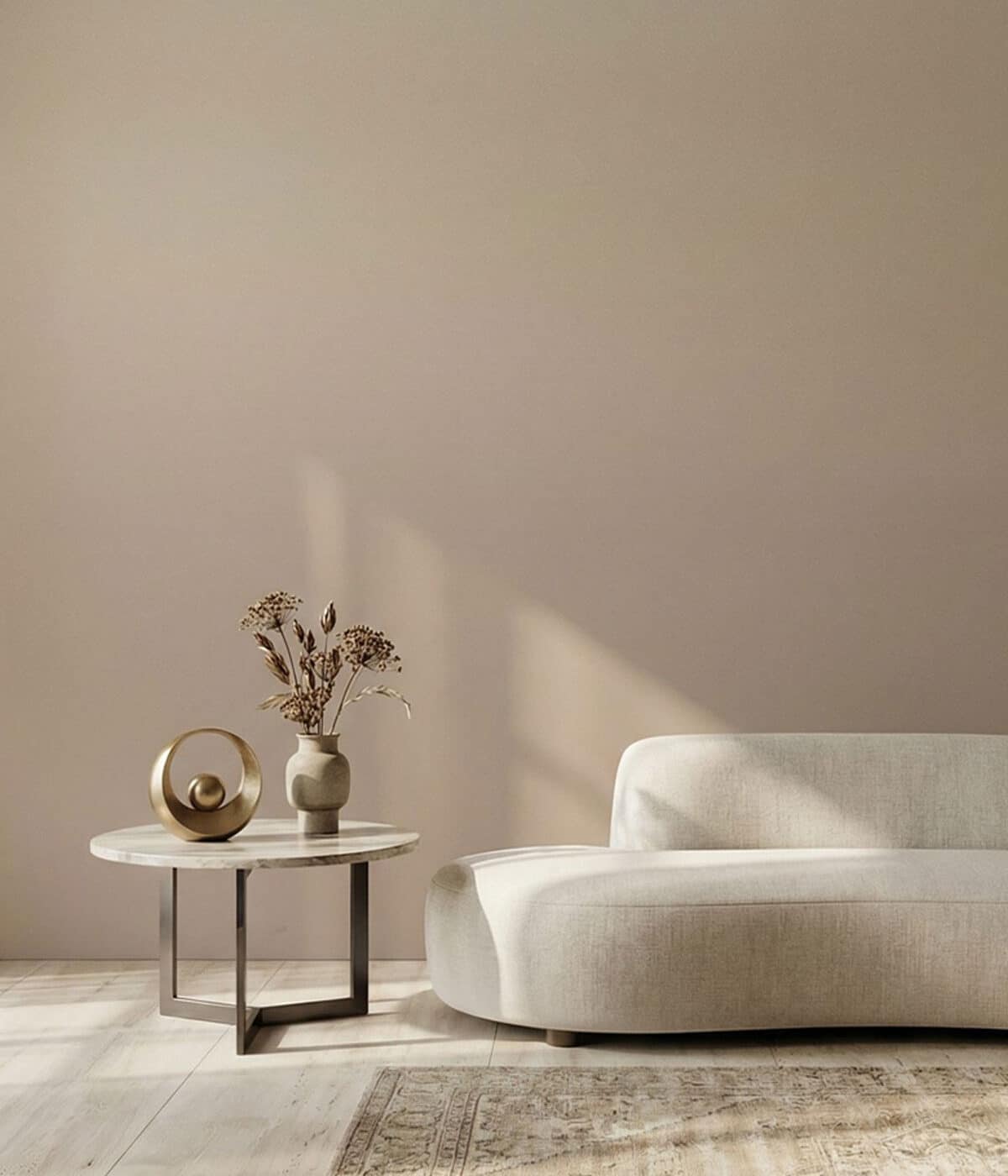 A minimalist living room featuring soft brown and cream ombre wallpaper that fades gently across the wall. A curved cream sofa sits beside a marble-top side table with a decorative sculpture and dried flowers, bathed in warm natural light.