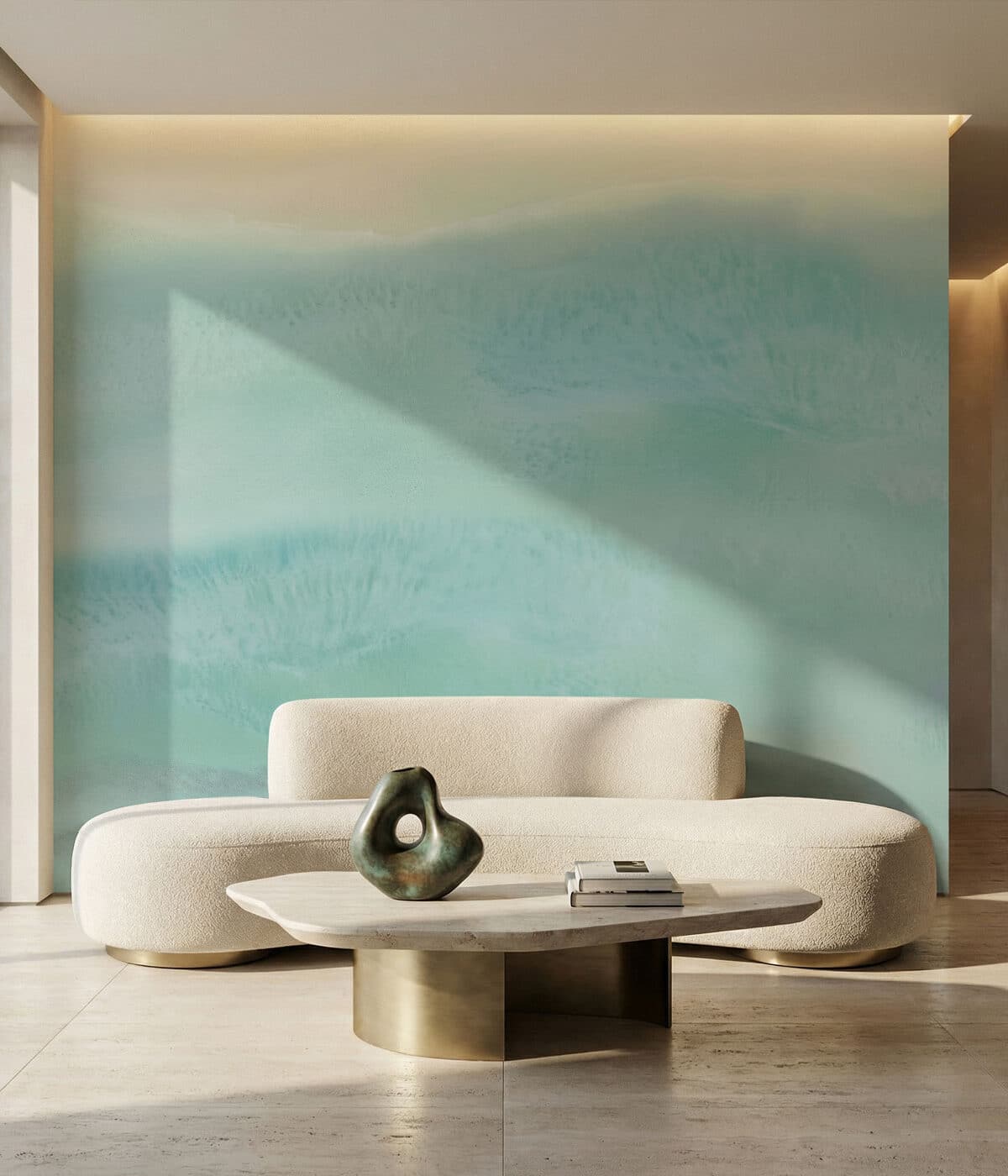 A modern living room featuring a curved cream boucle sofa with brass base accents set against a soft blue and pale yellow gradient wall mural that resembles an abstract ocean shoreline. In front of the sofa sits a sculptural coffee table with a light stone top and a rounded brass base, holding a green abstract ceramic sculpture and a small stack of books. Natural light casts diagonal shadows across the wall and floor, creating a calm, coastal-inspired atmosphere.